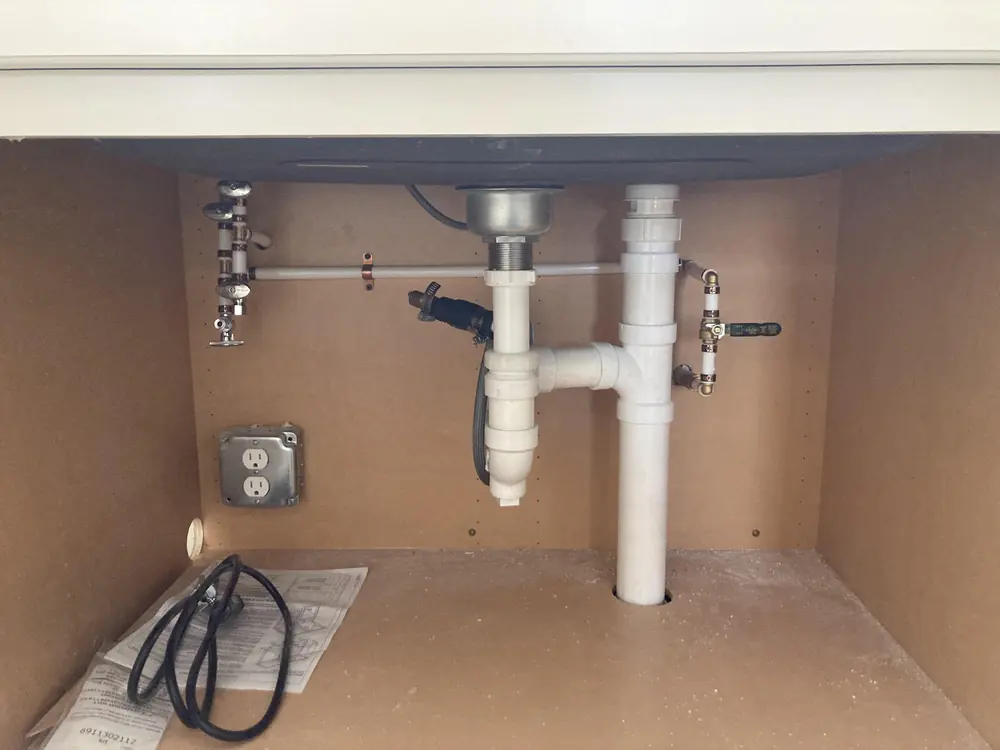 Shut-off valves and supply lines visible under a sink with the cabinet opened