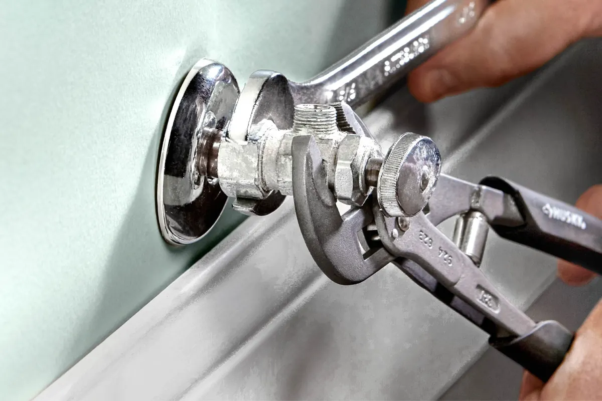 Plumber tightening a trap fitting with tongue and groove pliers