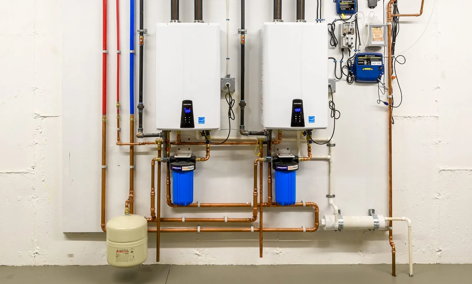 Two tankless water heaters mounted on a wall with copper manifold piping